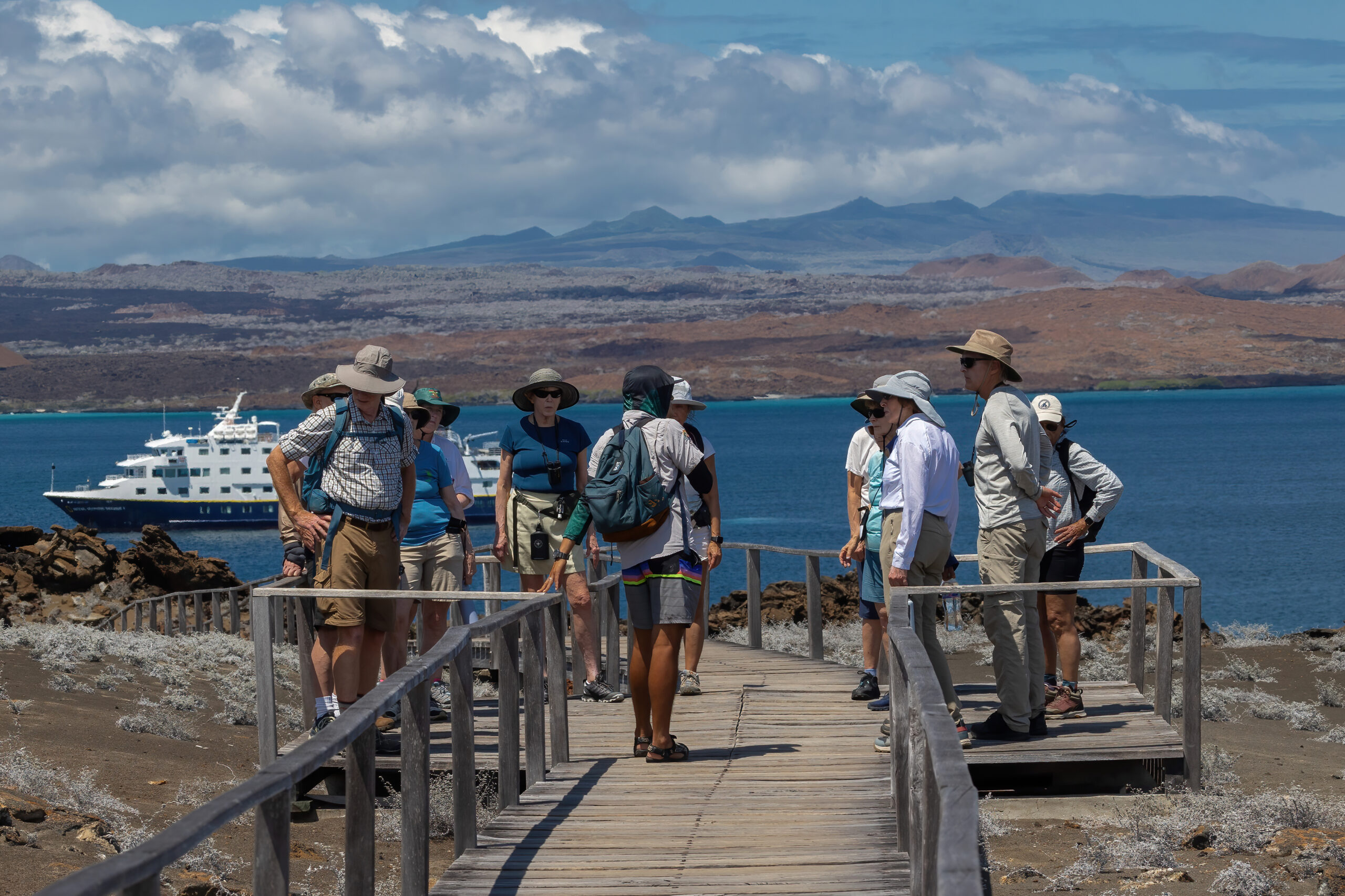 Travelers at a Galapagos viewpoint with an expedition vessel in the background