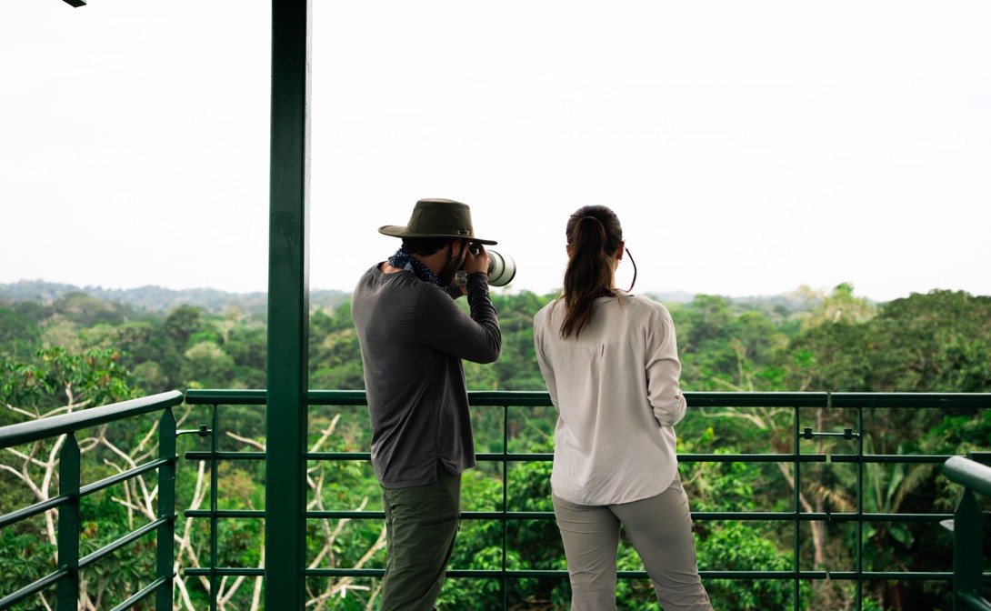Travelers observing the rainforest from a lodge balcony